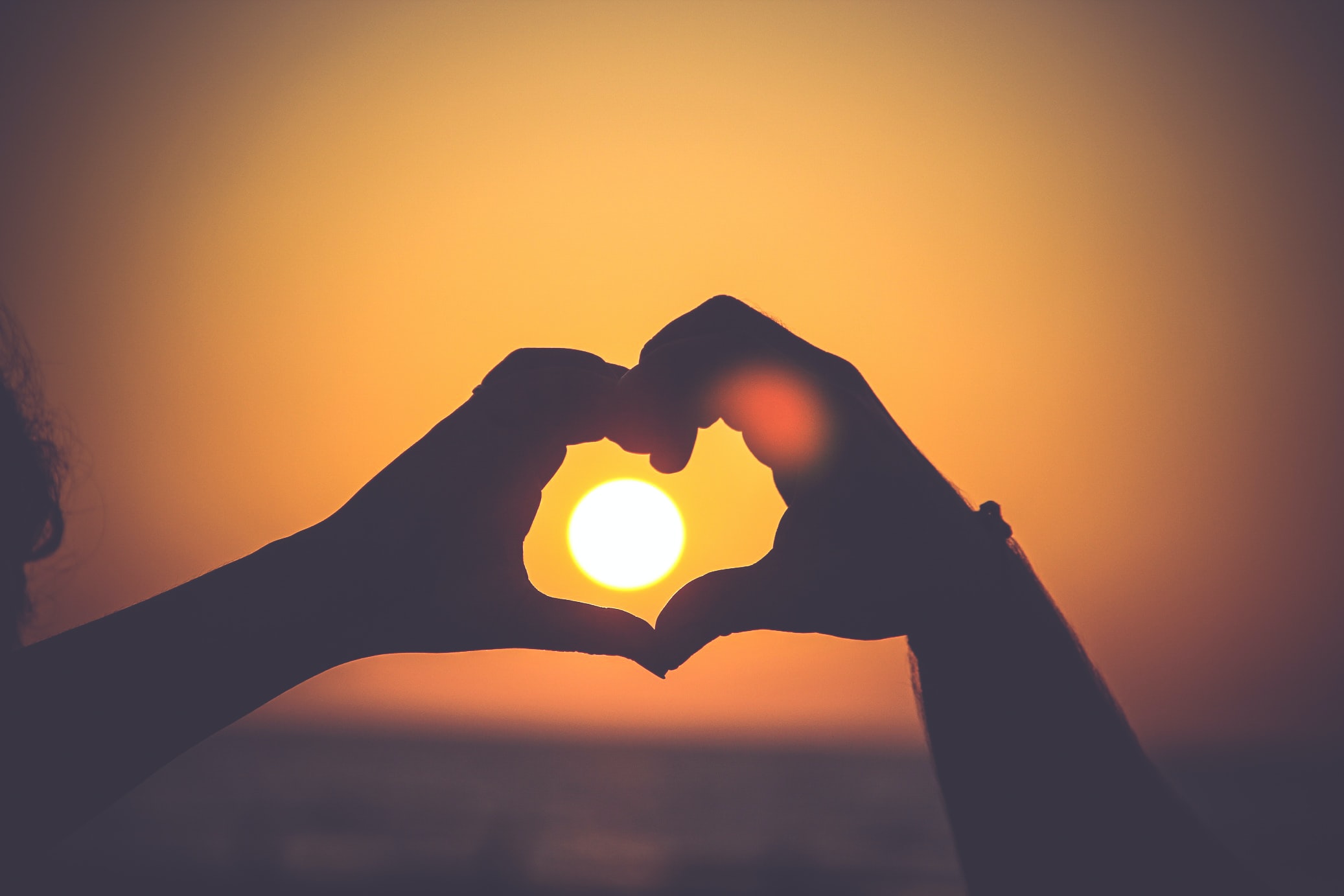 Hands forming a heart shape with sunset in background