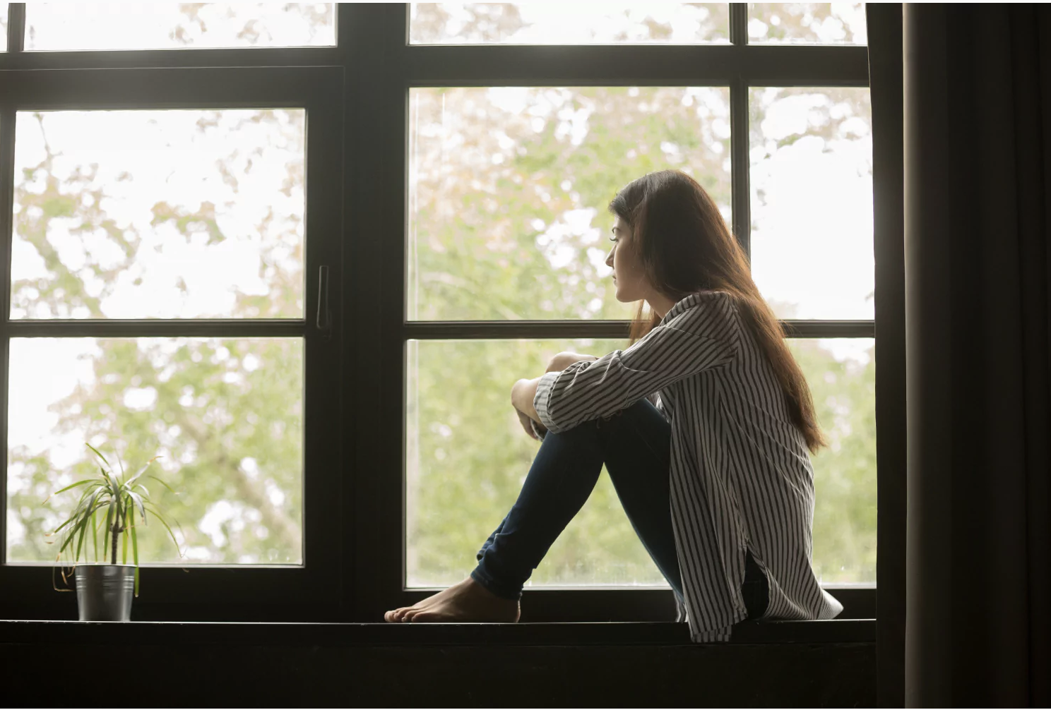 A teenager sits by a window looking outside, lost in thought. Child and teen suicide is a leading cause of death, and it's vital that we know our children and how to prevent death by suicide.